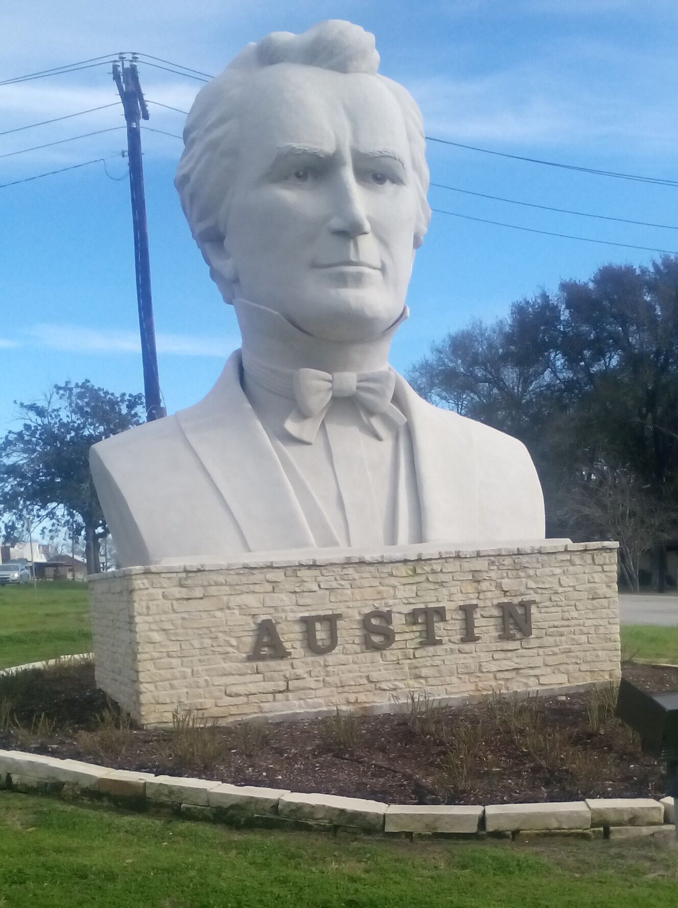 Une sculpture en buste représentant un homme portant un nœud papillon, placée sur un piédestal en pierre sur lequel est gravé le mot « AUSTIN ».