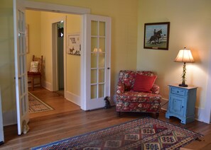 A room with a wooden floor, a red floral sofa, a blue cabinet, and a patterned rug.