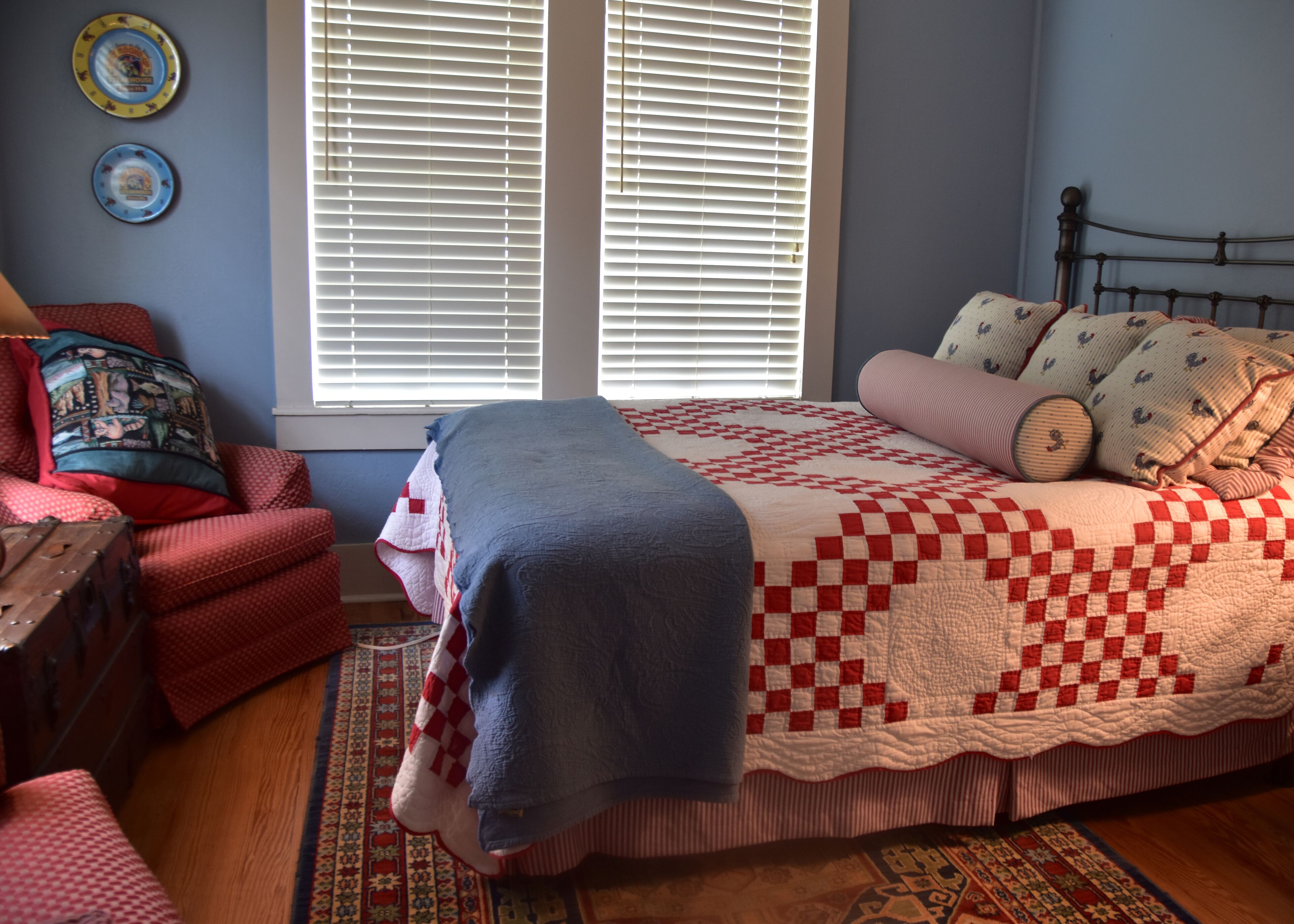 Une chambre à coucher comprenant un lit, une chaise, une fenêtre avec des stores et un mur orné de deux assiettes décoratives.