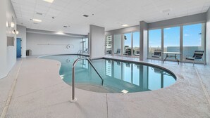 Ein Innenpool mit klaren Glaswänden, einem geschwungenen Design und Blick auf die Skyline der Stadt durch große Fenster.