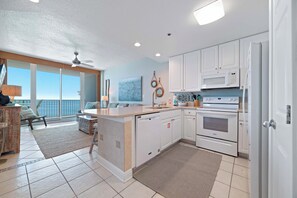 A modern kitchen with white cabinets, a microwave, an oven, and a dishwasher. There is a large window providing a view of the outdoors.