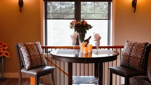 A dining area with a round table, two chairs, a vase with flowers, candles, and a window with a view of trees. - Chalet Style Suite on Peachland Acreage (Peachland)