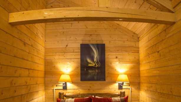 Une chambre confortable, aménagée dans un chalet en bois, avec un lit, deux lampes de chevet et un tableau accroché au mur.