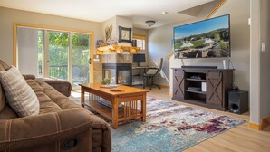 Una sala de estar con sofá, mesa de centro, chimenea, televisor y un amplio ventanal con vistas a un jardín.