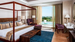 A spacious hotel room with a four-poster bed, a sitting area with a chair, a desk, and a view of a pool and greenery. - Three bed loft at Private Residence Club (Playa del Carmen)
