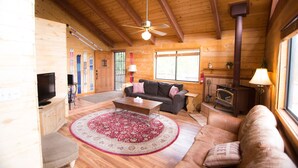 A cozy cabin interior with a wooden ceiling, a fireplace, a sofa, a coffee table, and a television.
