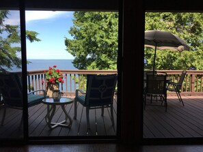 A deck with a table and chairs, a potted plant with red flowers, and a view of the ocean. - Lovely, Open Cottage on Lake Ontario (Henderson)