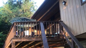 A wooden deck with a railing, a covered seating area, and a staircase leading to an upper level.