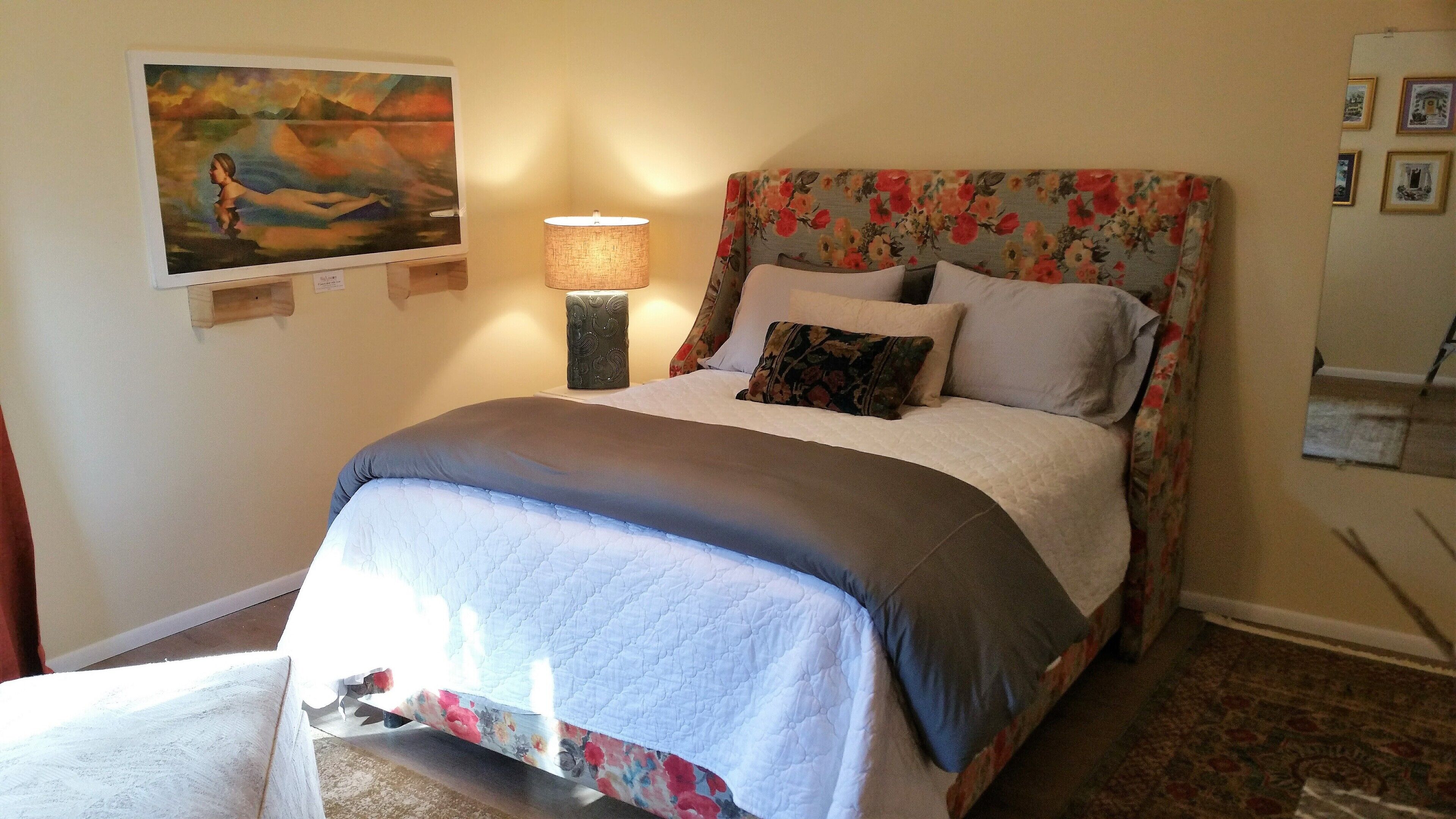 A bedroom with a bed, a nightstand, a lamp, and a painting on the wall.