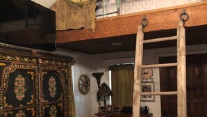 Een kamer met een houten plafond, een ladder, een decoratieve kast, een gele fauteuil en een wandklok.