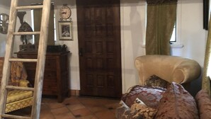 Een kamer met een houten ladder, een bruine deur, een beige fauteuil en decoratieve kussens.
