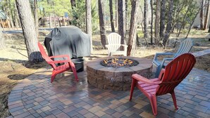 Un patio con sillas rojas, un hoyo para fuego y una parrilla cubierta.