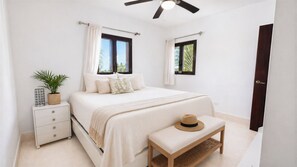 Une chambre à coucher avec un lit, des tables de chevet, un ventilateur de plafond et des fenêtres avec des rideaux.