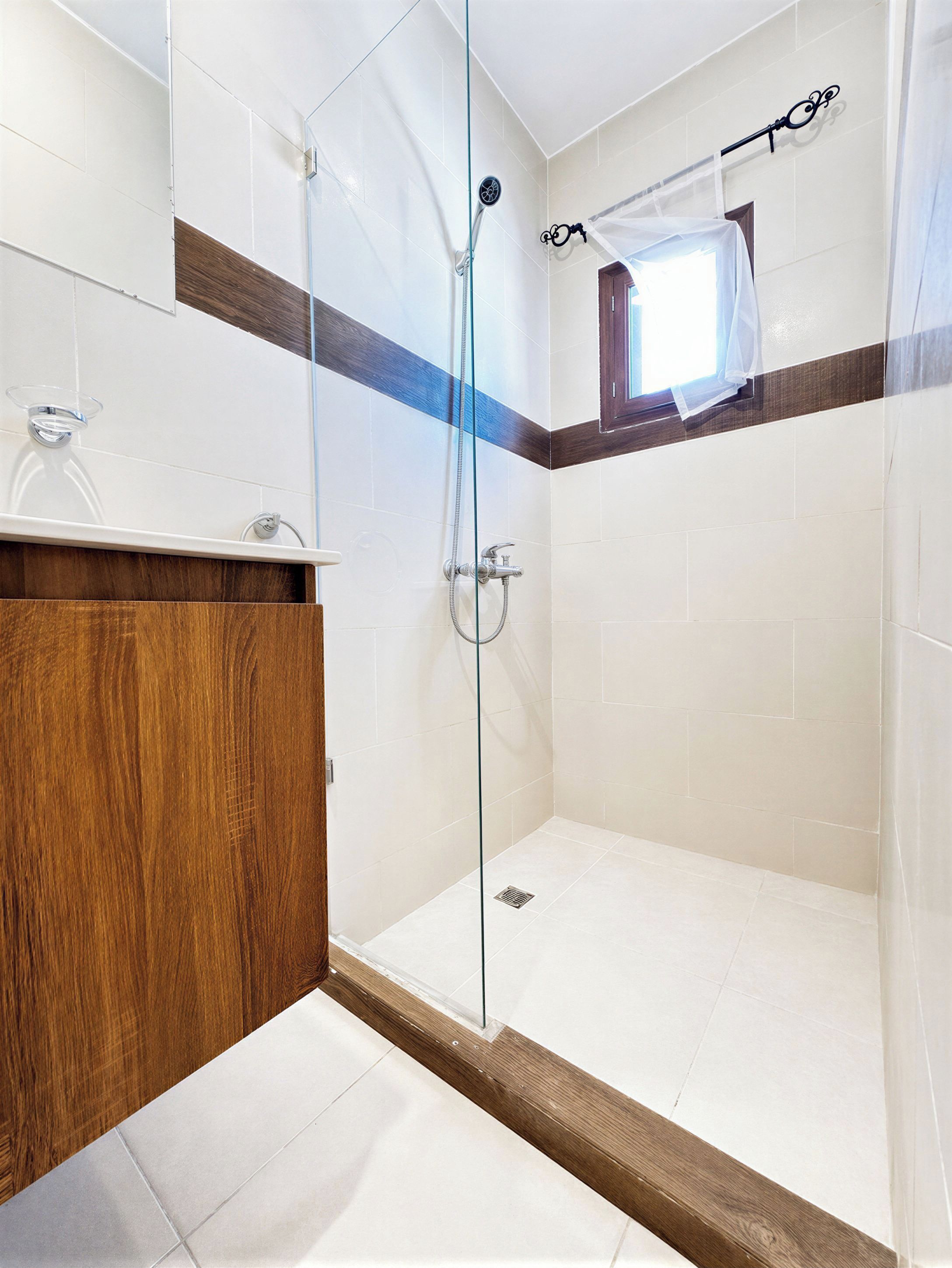 Een moderne badkamer met een douchecabine van glas, een houten wastafelmeubel en een klein raam.