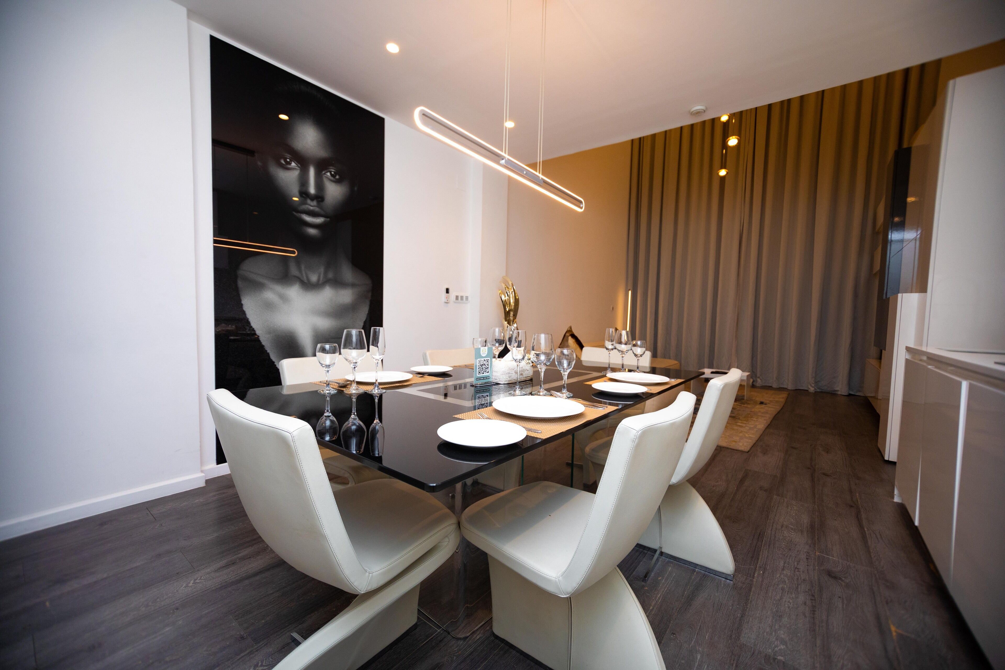 A modern dining area with a long table, white chairs, and a large abstract painting on the wall.