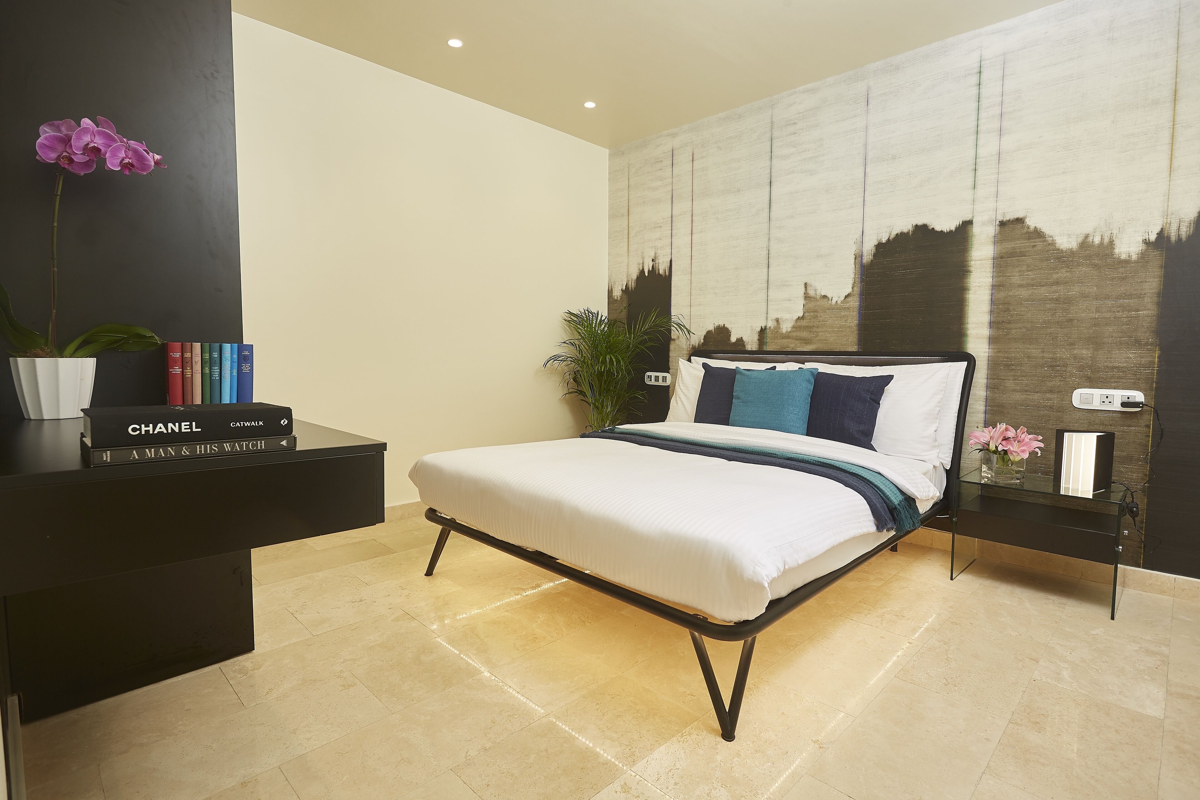A modern bedroom with a bed, bedside tables, a bookshelf, and a cityscape painting on the wall.
