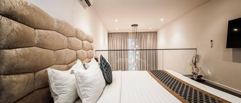A modern hotel room with a large bed, a headboard, a flat-screen TV, and a window with curtains.