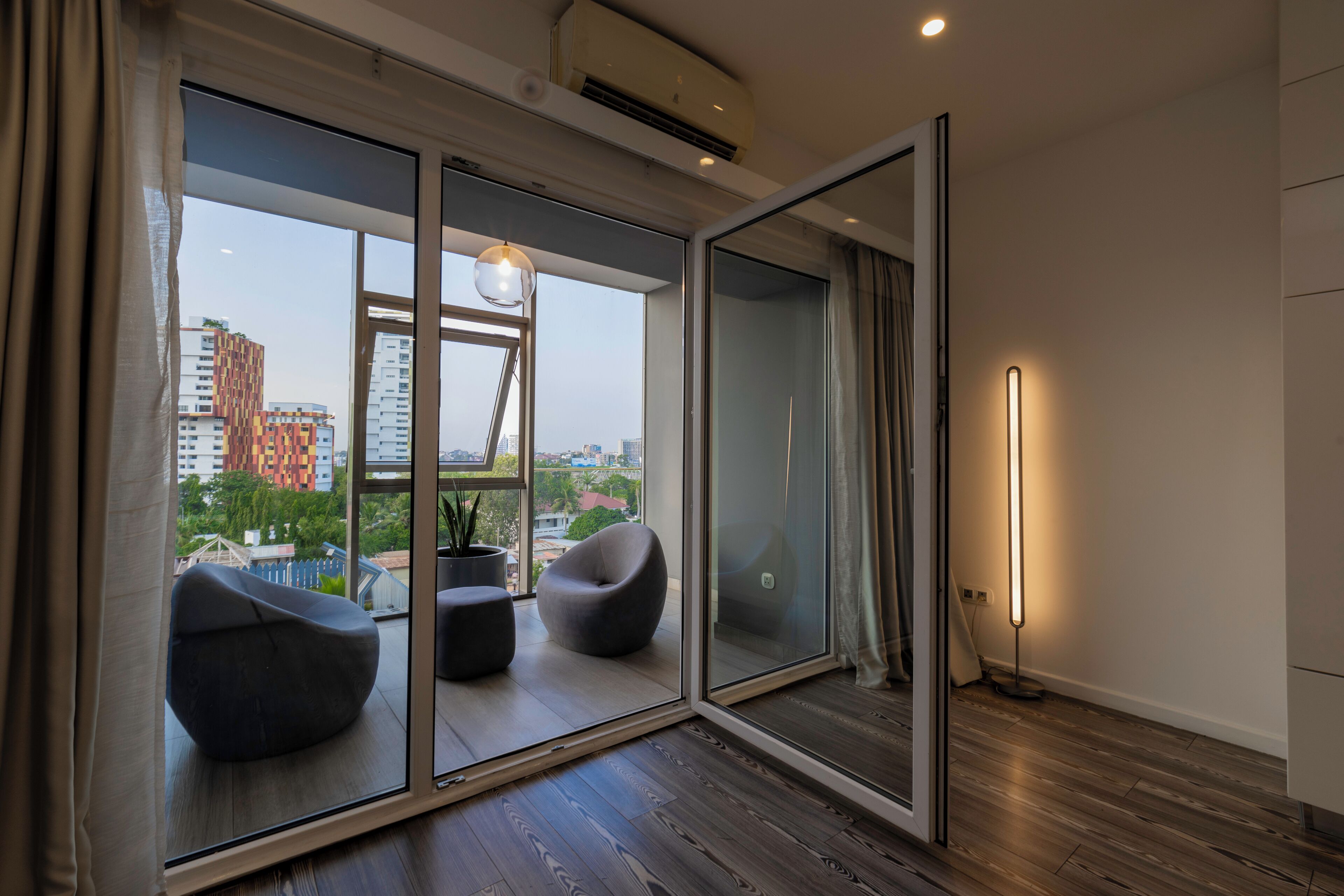 A modern room with a large sliding glass door leading to an outdoor balcony, a standing floor lamp, and a potted plant.