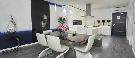 A modern kitchen with white cabinets, a black door, and a dining area with a glass table and white chairs.