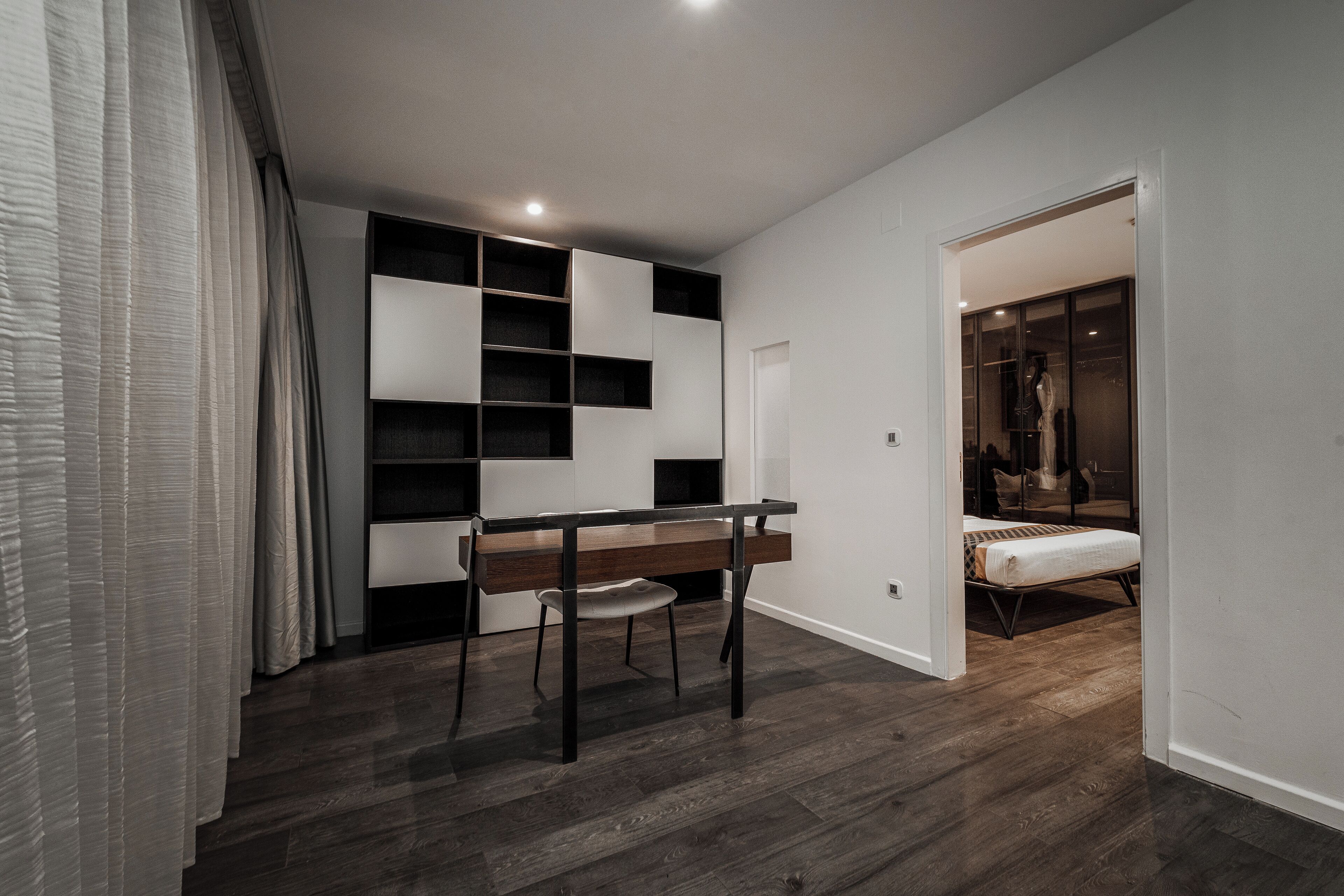 A modern bedroom with a wooden desk, a chair, a bed, and built-in shelving.