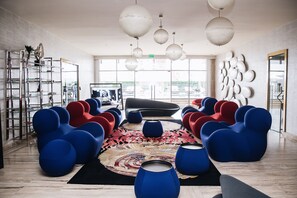 A modern lounge area with blue and red seating, a patterned rug, and a large window offering a city view.
