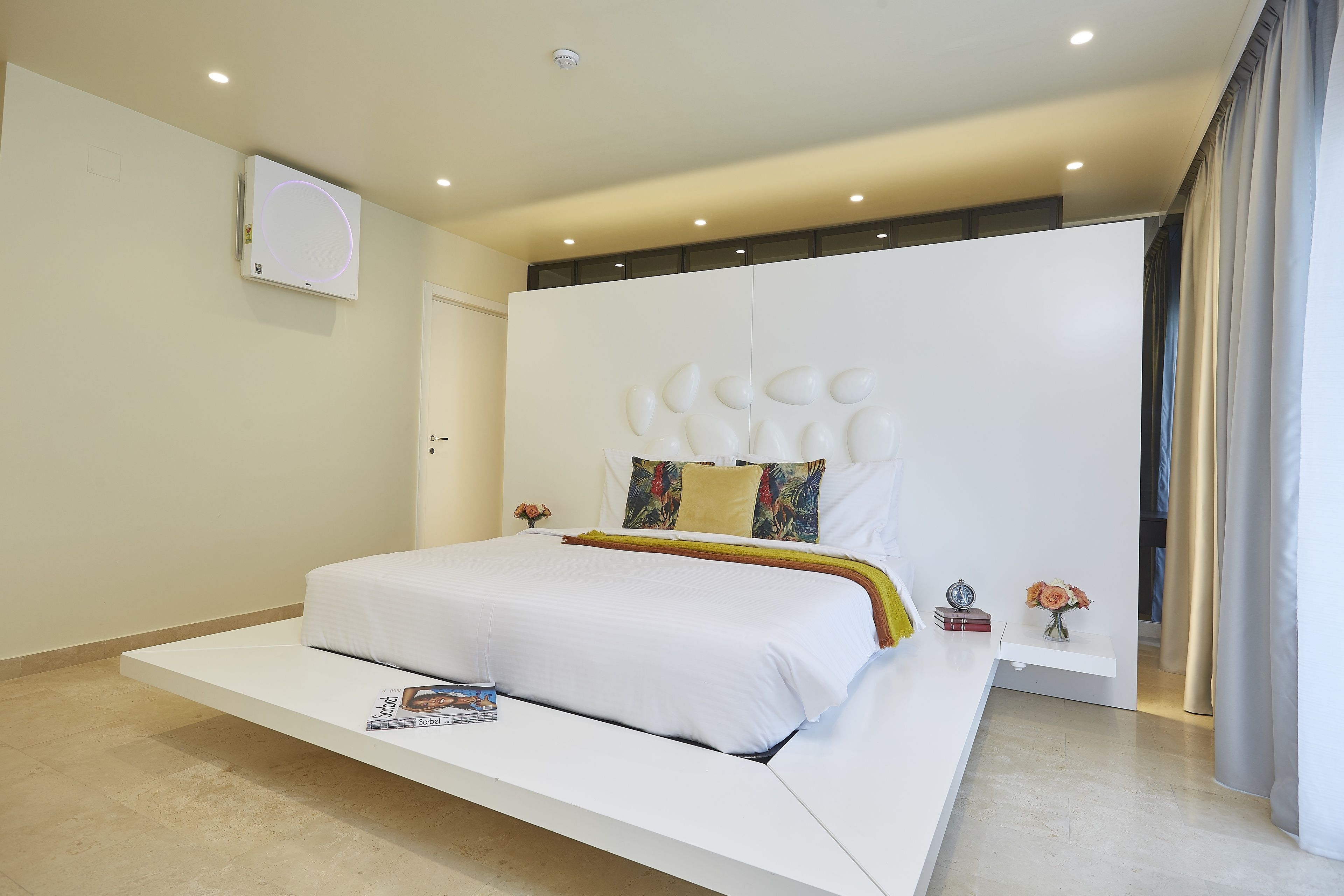 A modern bedroom with a large bed, a white headboard, and a small bedside table with a vase of flowers.