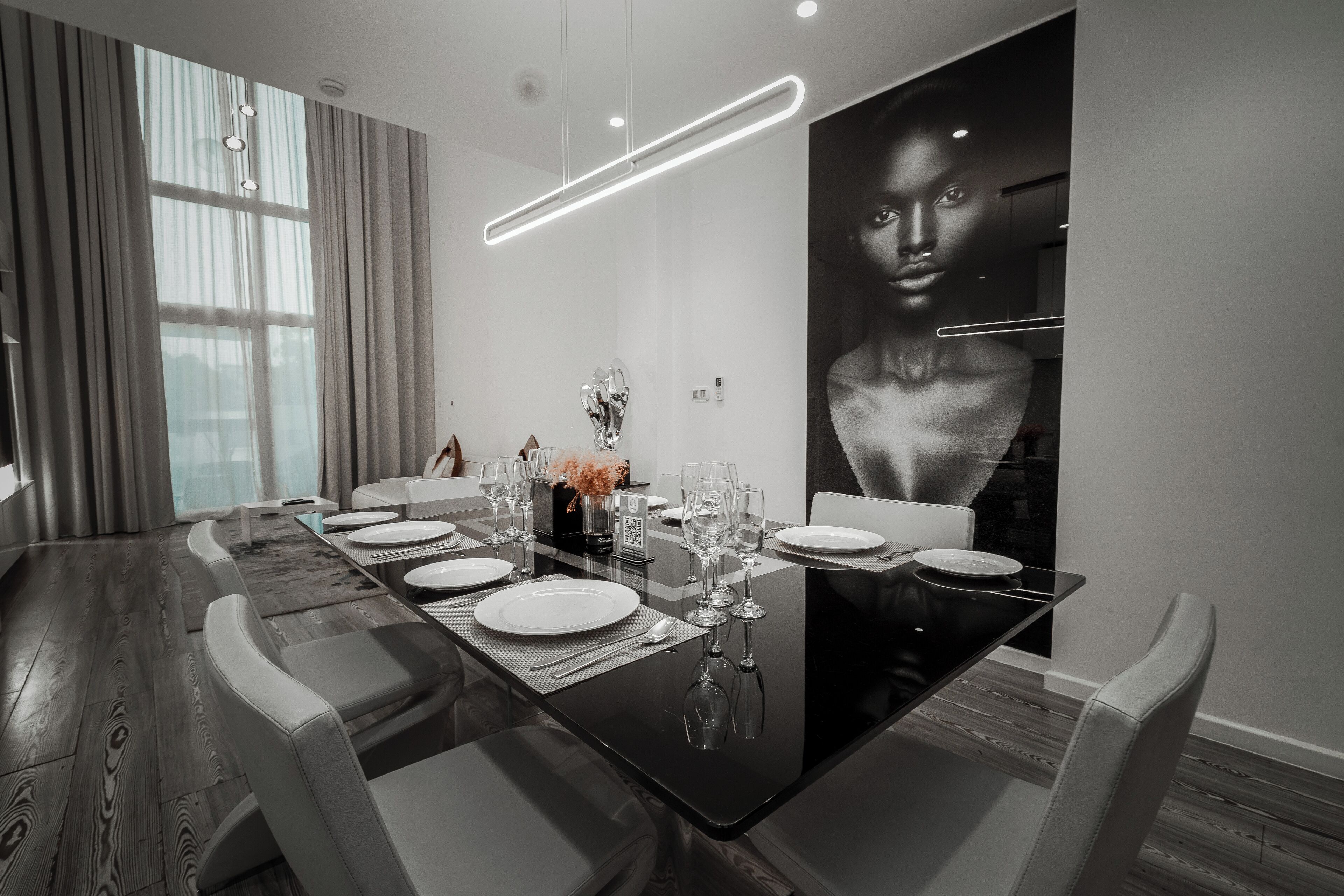 A modern dining area with a long table set for six, featuring a sleek black table, white chairs, and a large abstract painting on the wall.