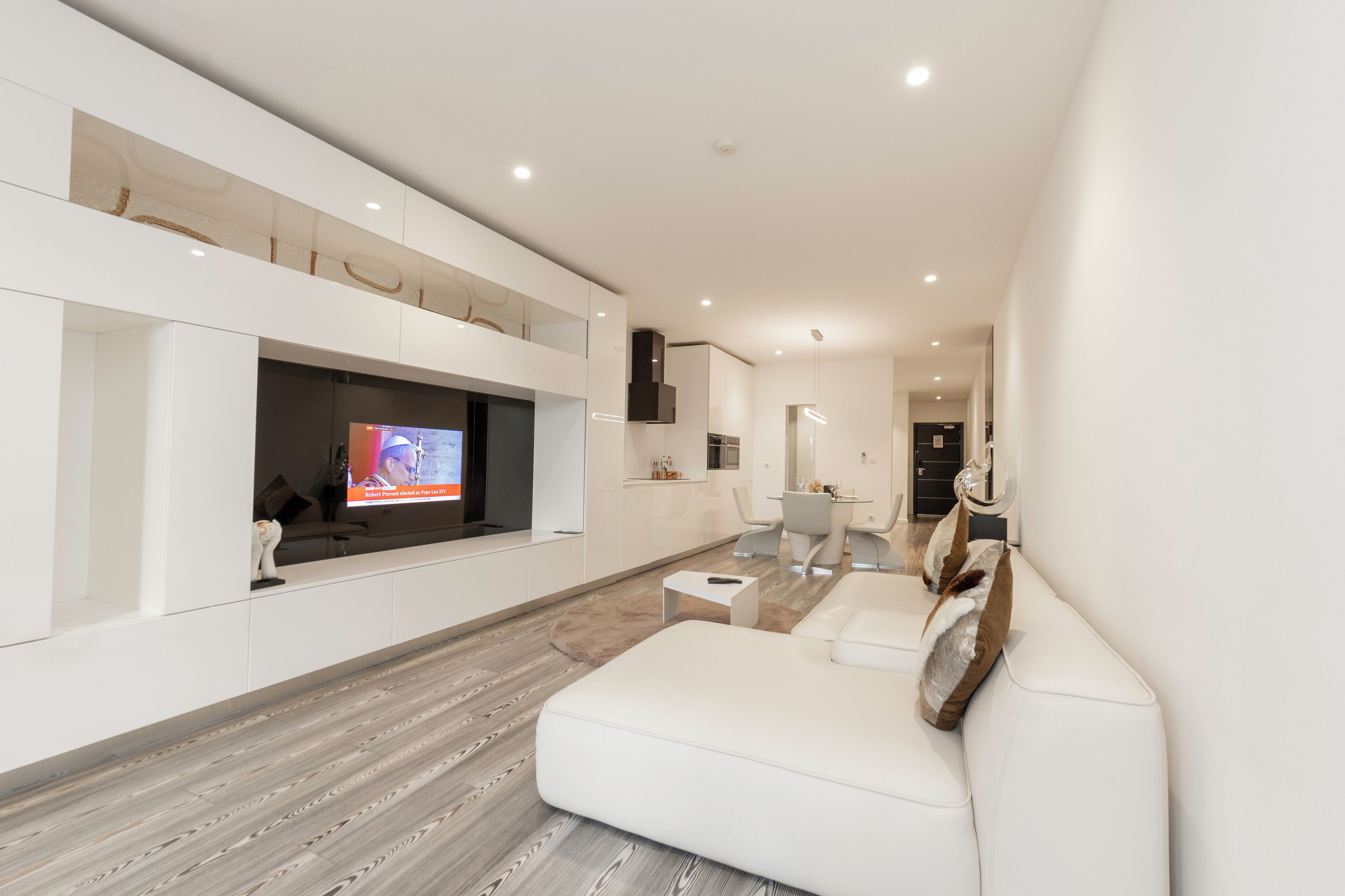 A modern living room with a flat-screen TV, white sofas, a coffee table, and a wooden floor.