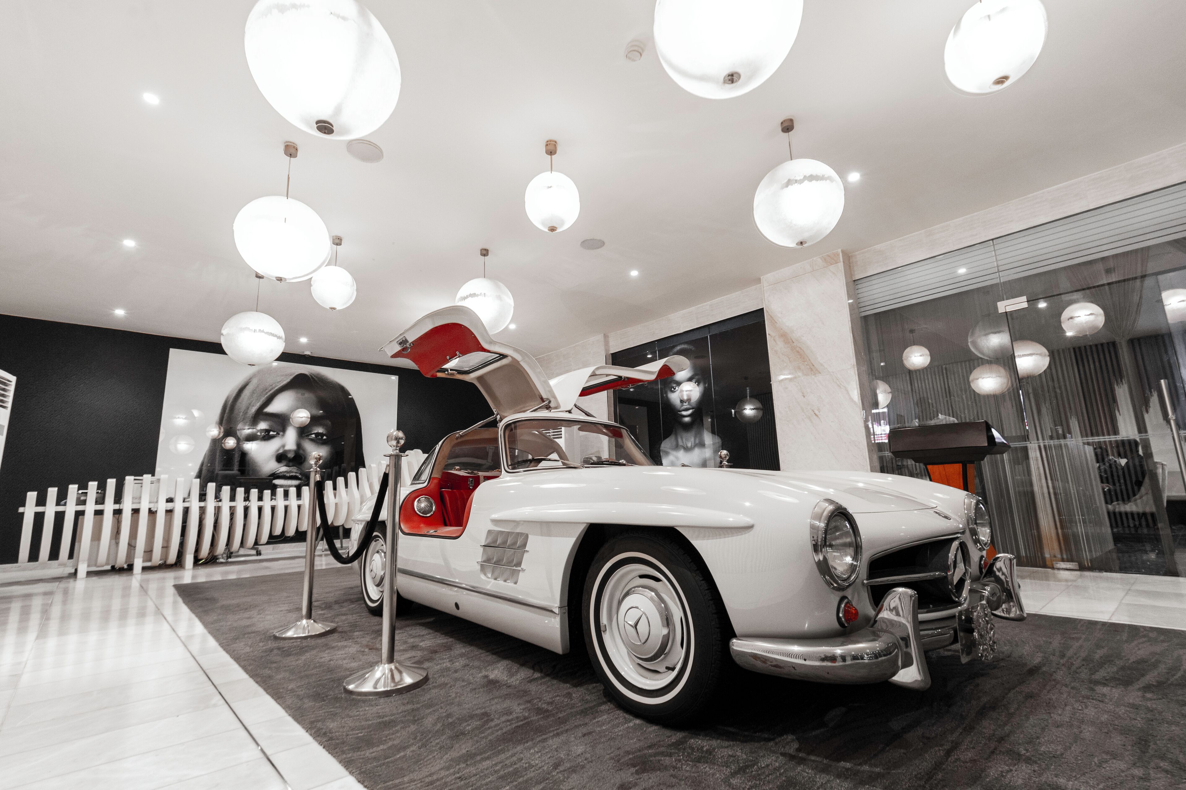 Een witte oldtimer met openstaande deuren, binnenshuis gepresenteerd met meerdere hangende bolvormige lampen.