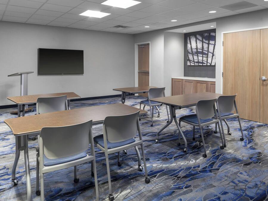 A conference room with a large table, chairs, a projector screen, and a carpeted floor.