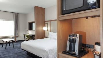 A hotel room with a bed, a desk, a chair, a microwave, and a coffee maker.