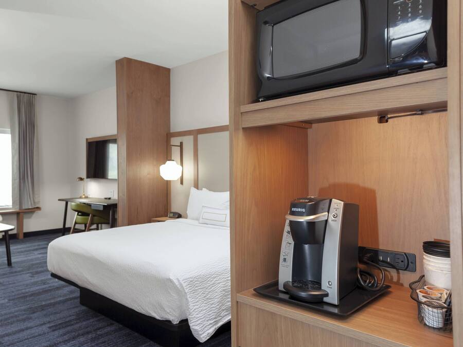 A hotel room with a bed, a desk, a chair, a microwave, and a coffee maker.