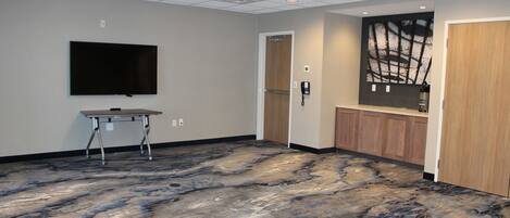 A conference room with a large flat-screen TV, a wooden door, and a patterned floor.