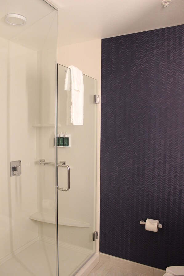 Une salle de bain moderne avec une douche à parois de verre, des toilettes blanches et un mur à motifs sombres.