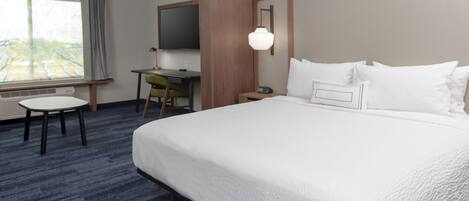 Habitación de hotel con una cama grande, un escritorio, una silla, un televisor y una ventana con cortinas.