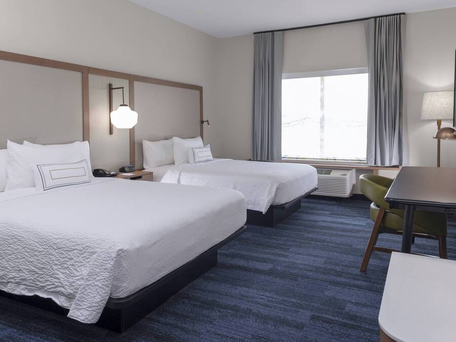 Habitación de hotel con dos camas, un escritorio, una silla, un televisor y una ventana con cortinas.