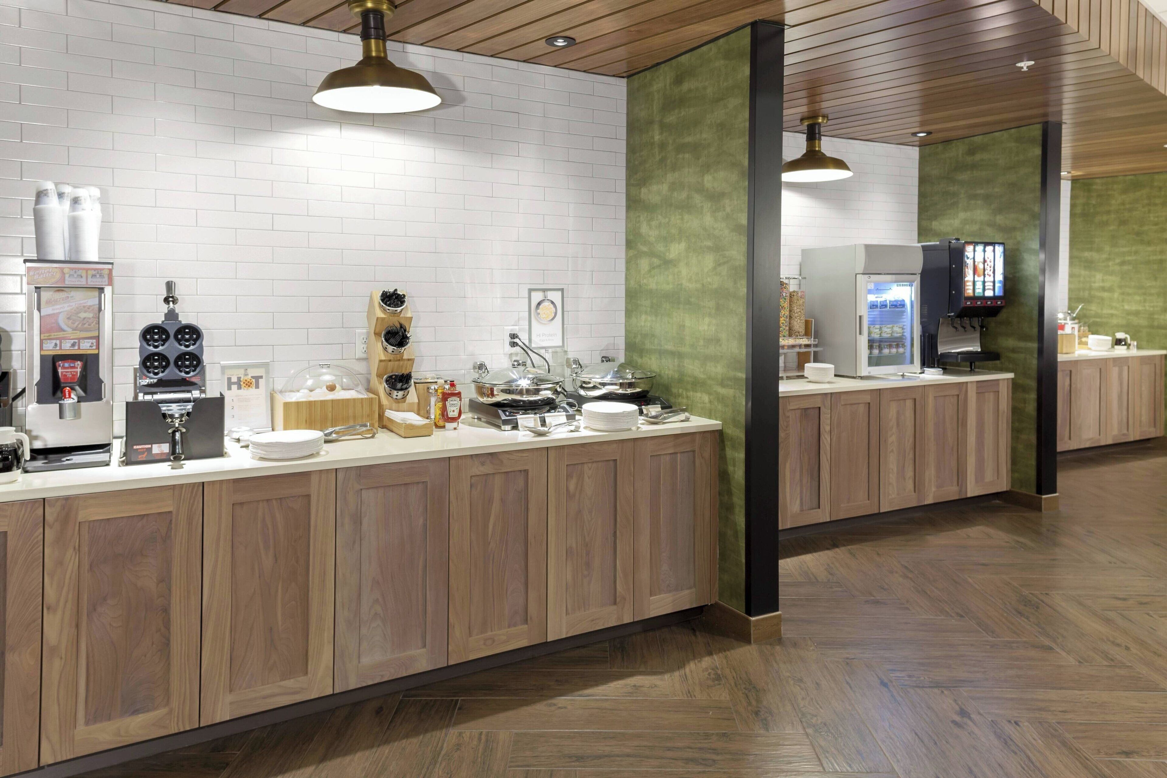 A modern kitchen area with a long counter, various appliances, and a green accent wall.