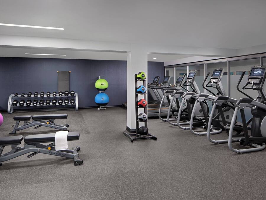 Un gimnasio con cintas de correr, bancos de pesas y pelotas de ejercicios.