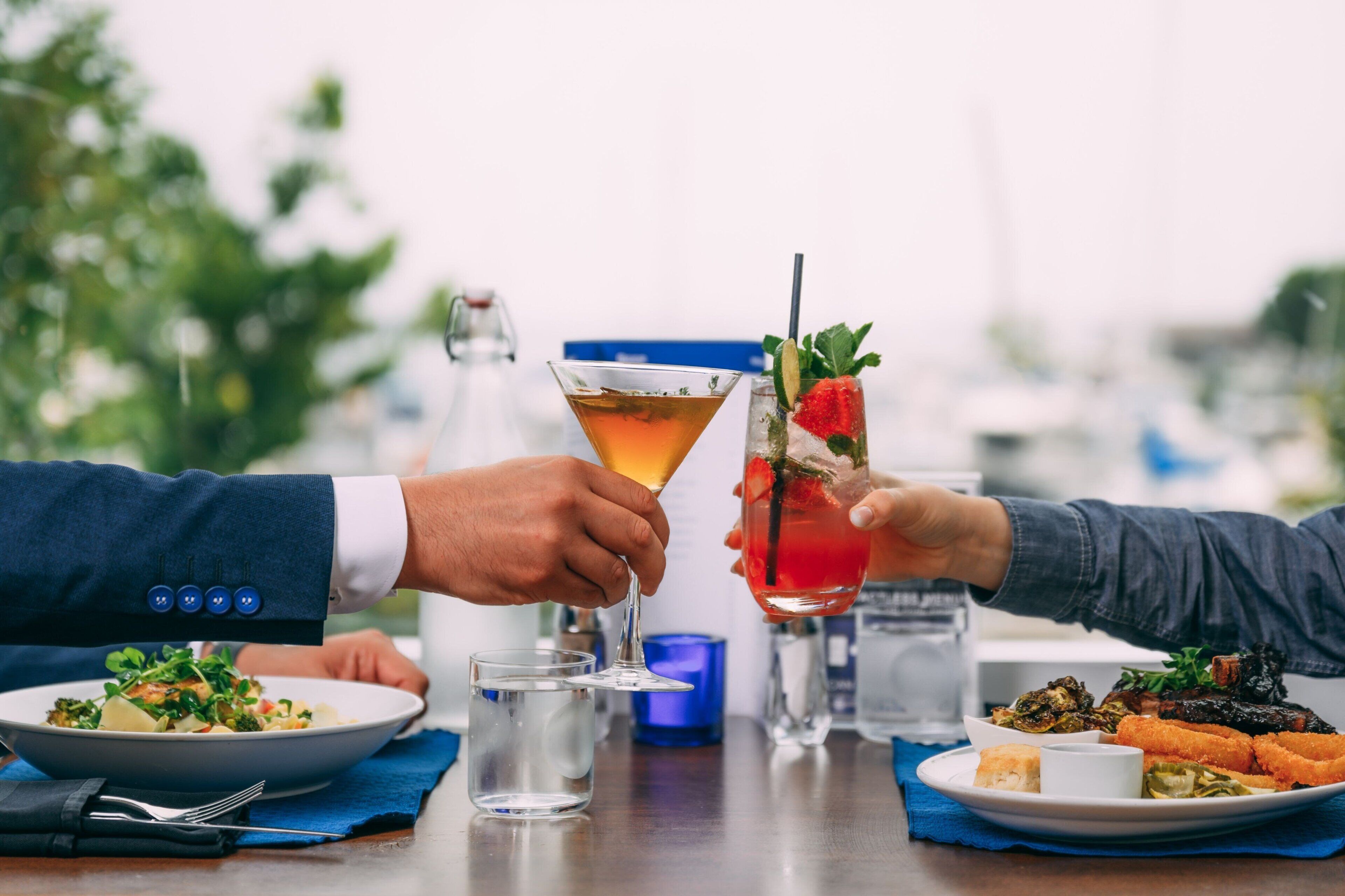 A dining table with a meal, a martini glass, and a cocktail glass.