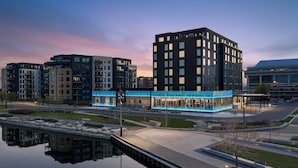 Ein modernes Stadtgebiet mit hohen Gebäuden, einem spiegelnden Wasserspiegel und einem gut beleuchteten Fußweg.