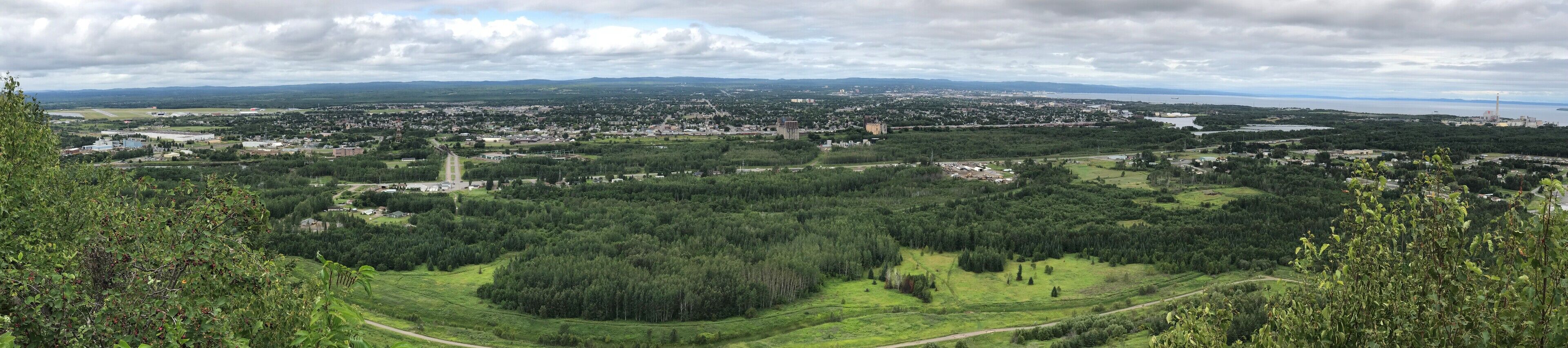 Vista panorámica de un pueblo con zonas residenciales e industriales, rodeado de vegetación y una masa de agua en la distancia.