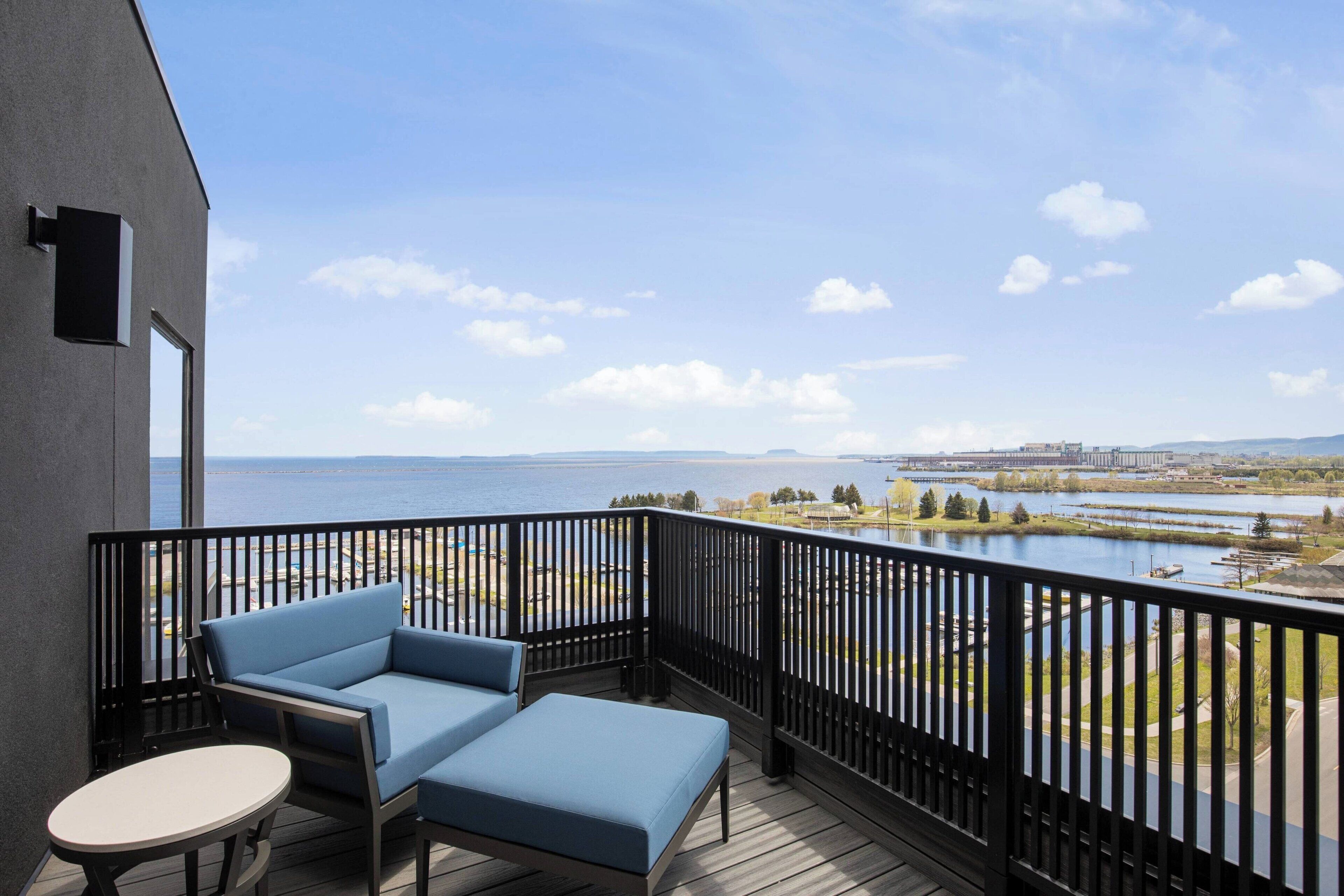 A balcony with a view of a lake and distant cityscape, furnished with a sofa and a small table.