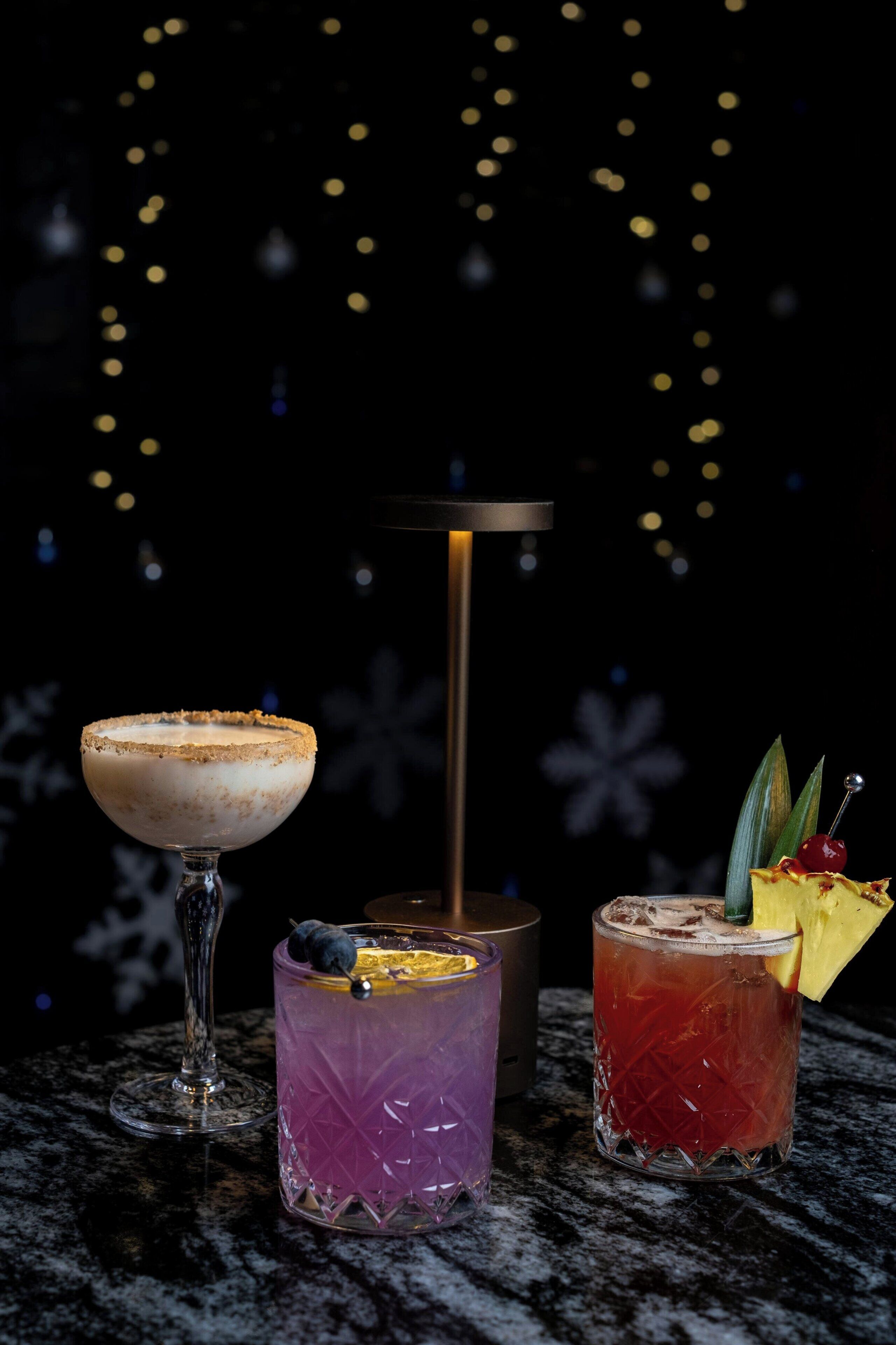 Three cocktails on a marble surface with a dark background and string lights.