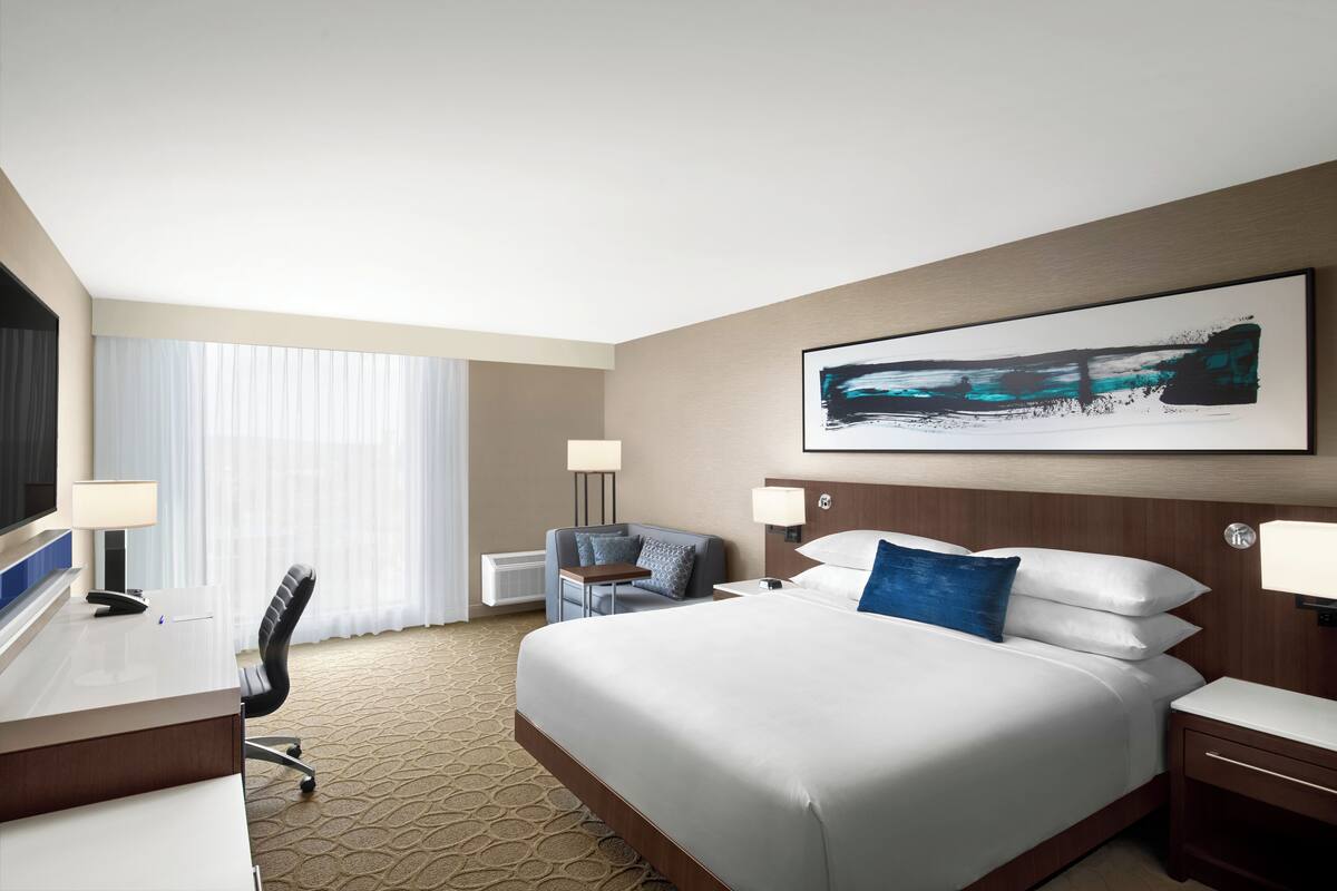 Une chambre d’hôtel avec un grand lit, un bureau avec une chaise, une télévision et un tableau au mur.
