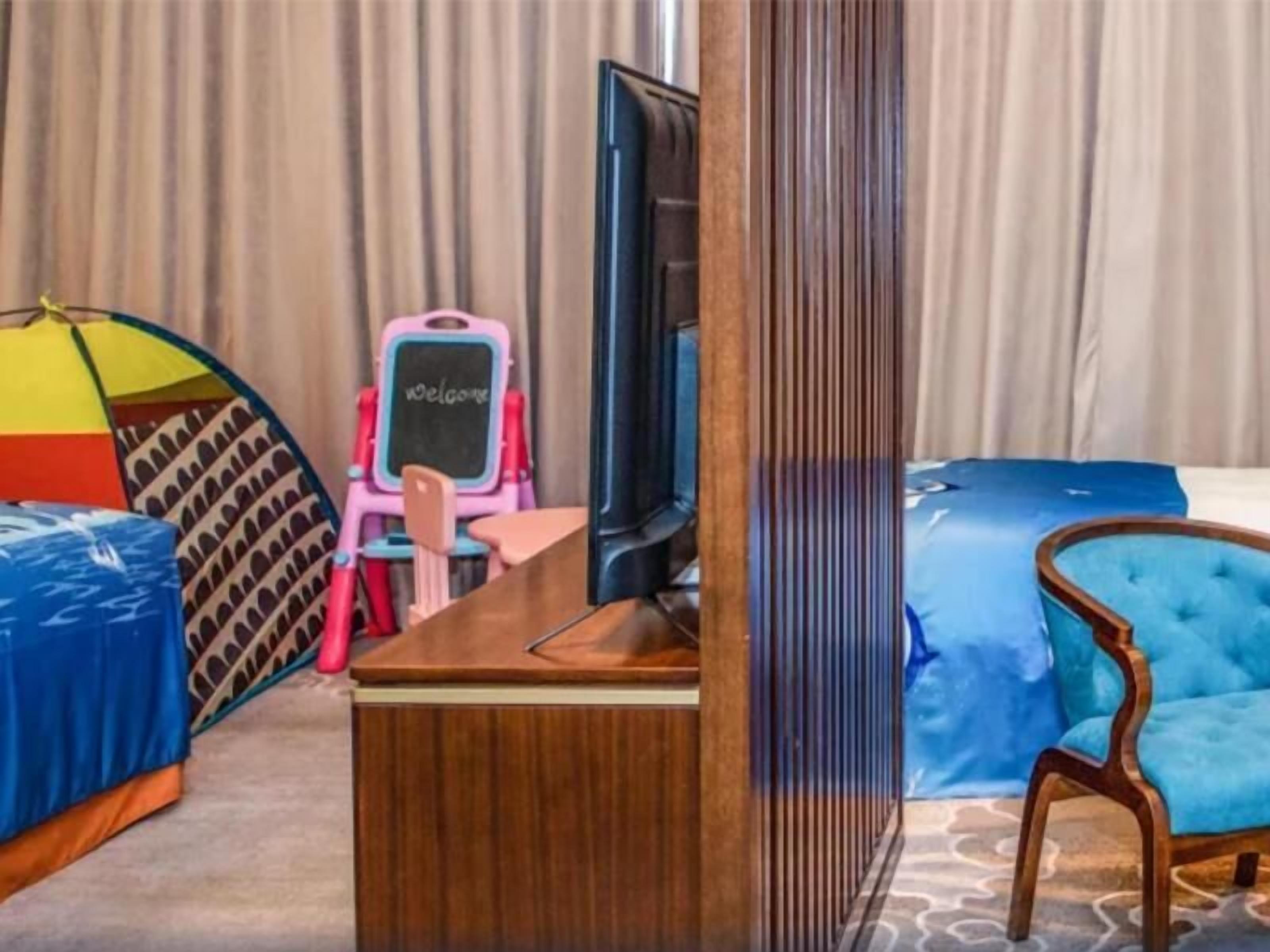 Una habitación de hotel con un escritorio de madera, un televisor, un sofá azul, una silla rosa y un paraguas colorido.