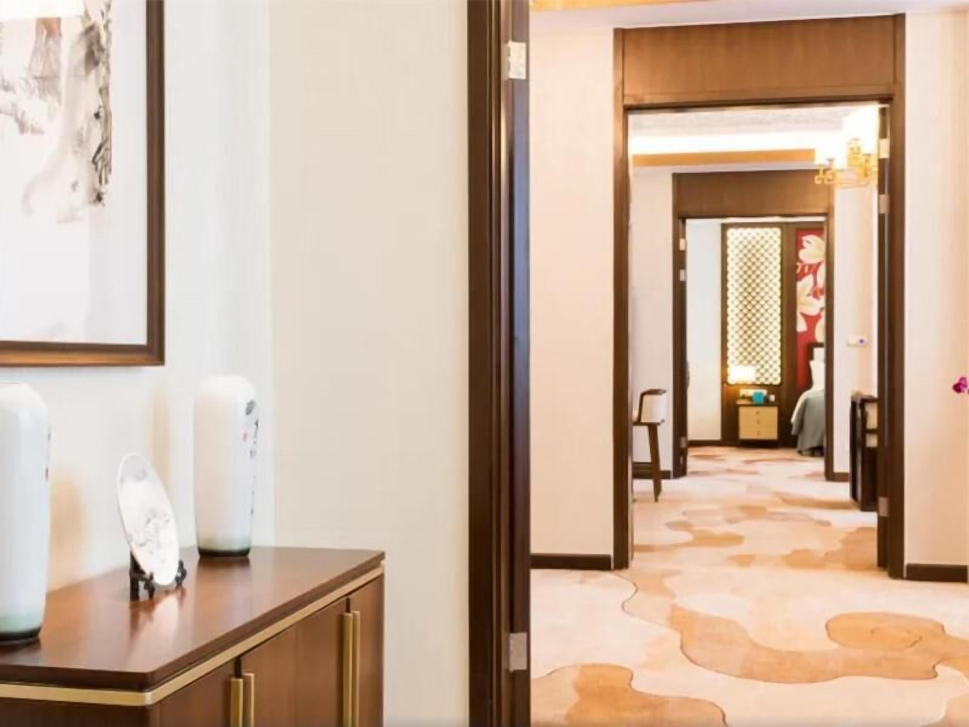 A hotel hallway with a wooden floor, a desk with a vase, and a framed picture on the wall.