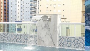 A swimming pool with a marble wall and a waterfall feature. - 100m da Praia Aviação Imperdível (Praia Grande)