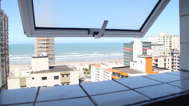 A view from a window overlooking a beach with buildings in the foreground. - 100m da Praia Aviação Imperdível (Praia Grande)