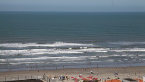 A beach with waves, people, and umbrellas. - 100m da Praia Aviação Imperdível (Praia Grande)