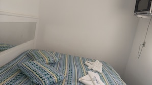 Une petite chambre avec un lit simple, une couvre-lit à motifs et une serviette blanche sur le lit.